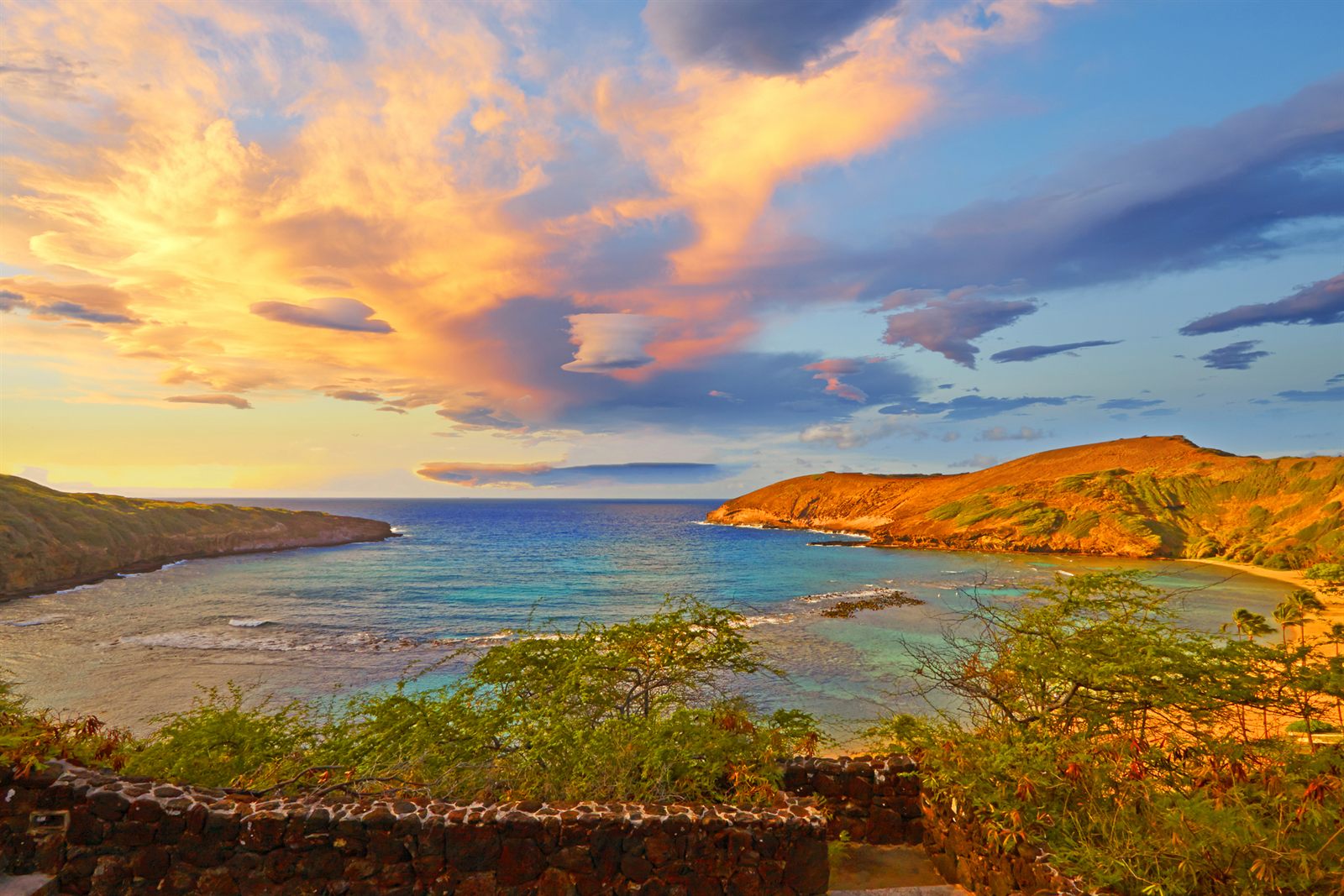 Storm clouds lit orange at sunset over a calm bay and rocky headland