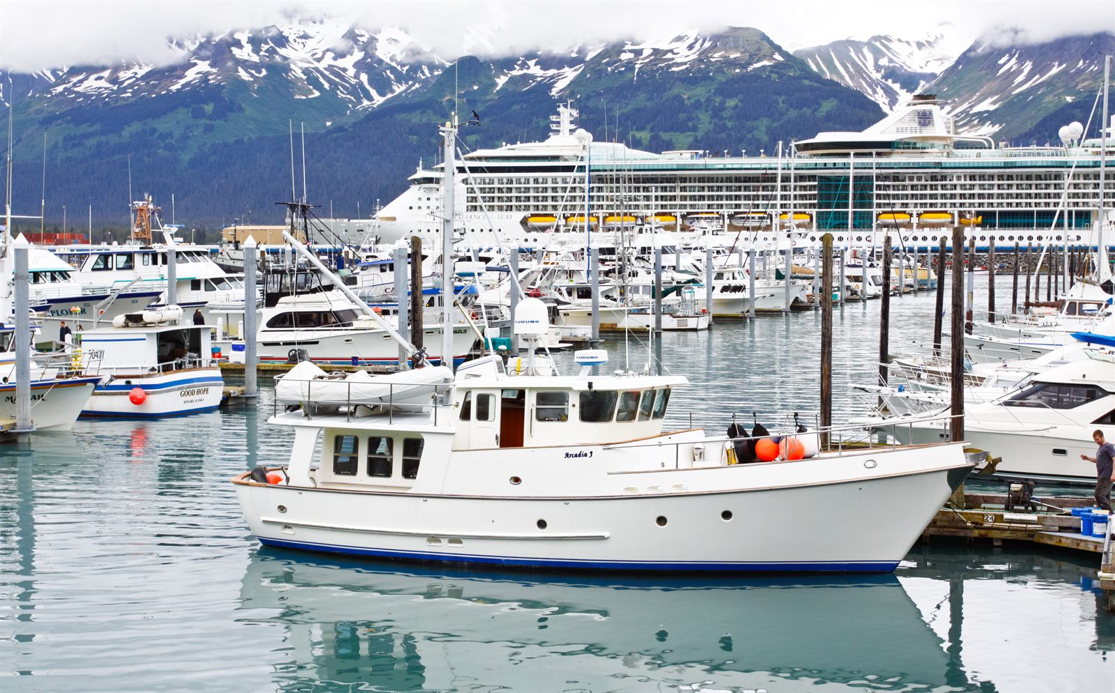 Cruise ship docked behind a busy marina of small boats below snowy mountains
